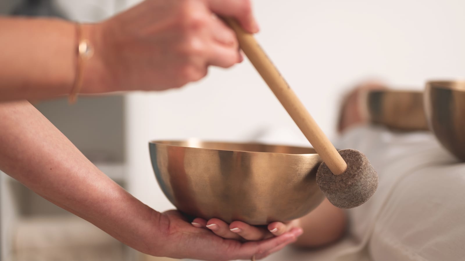 A close view of a Himalayan singing bowl with a wooden mallet resting beside it, soft amber light, the still register of a sound bath room before the session begins.